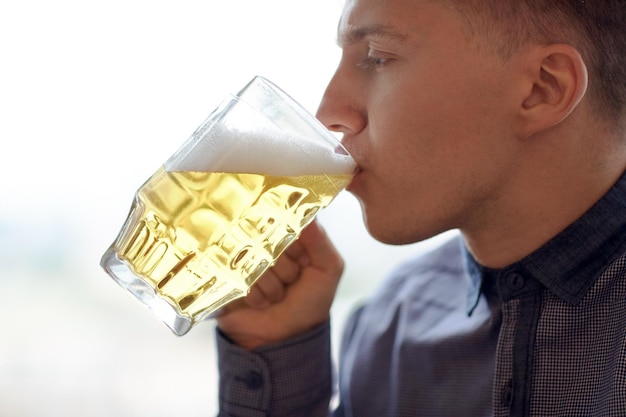 people, drinks, alcohol and leisure concept - close up of young man drinking beer from glass mug