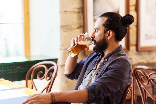 люди, напитки, алкоголь и концепция досуга - счастливый молодой человек пьет пиво из стекла в баре или пабе