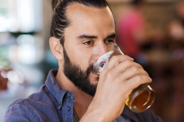 people, drinks, alcohol and leisure concept - happy young man drinking beer from glass at bar or pub