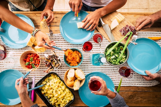 縦から見た食べ物でいっぱいのテーブルで友情や家族のお祝いで一緒に食べる人々