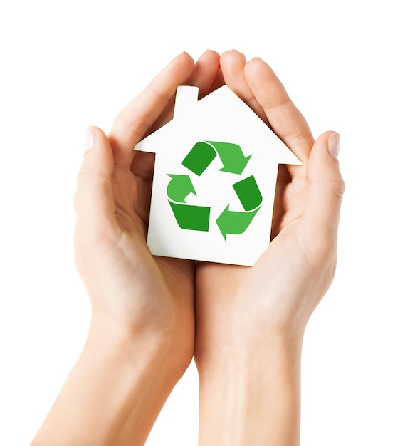 people, ecology, environment and conservation concept - close up of hands holding house with green recycling sign