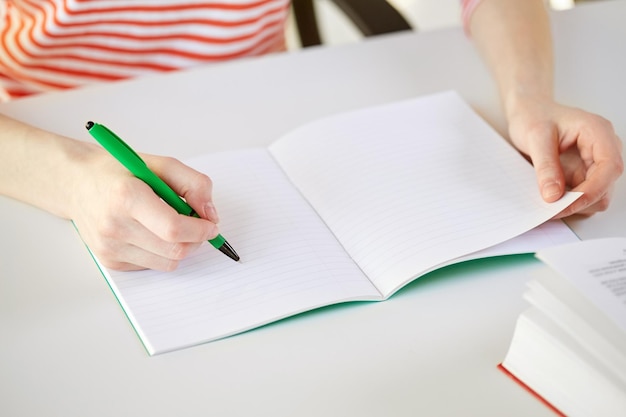 Concetto di persone e istruzione - primo piano delle mani femminili che scrivono sul taccuino a scuola