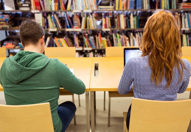 Foto persone, educazione e concetto di apprendimento - studenti con computer portatili e libri nella biblioteca scolastica