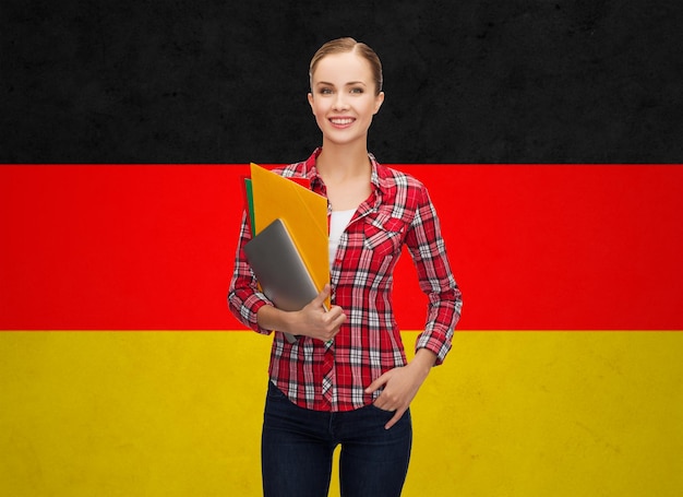 사람, 교육, 학습 및 학교 개념 - 독일 국기 배경 위에 태블릿 PC와 폴더가 있는 행복하고 웃는 10대 학생 소녀