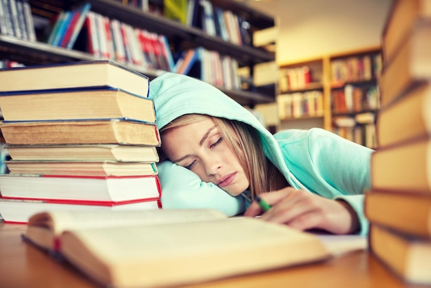 人、教育、セッション、試験、学校のコンセプト – 疲れた学生の女の子や、図書館で寝ている本を持つ若い女性