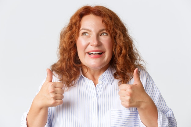 Foto persone, emozioni e concetto di stile di vita. primo piano di donna rossa eccitata e felice piena di emozioni positive, mostrando il pollice in su e guardando felice, consiglia qualcosa.