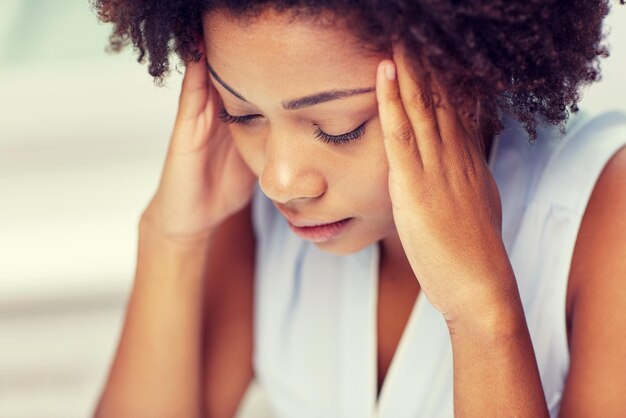 people, emotions, stress and health care concept - unhappy african american young woman touching her head and suffering from headache