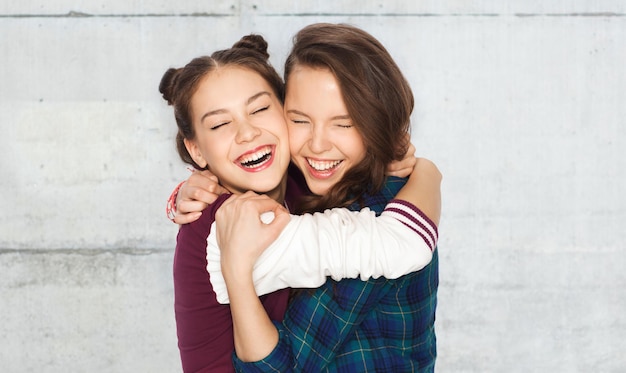 люди, эмоции, подростки и концепция дружбы - счастливые улыбающиеся симпатичные девочки-подростки обнимаются и смеются на фоне серой бетонной стены