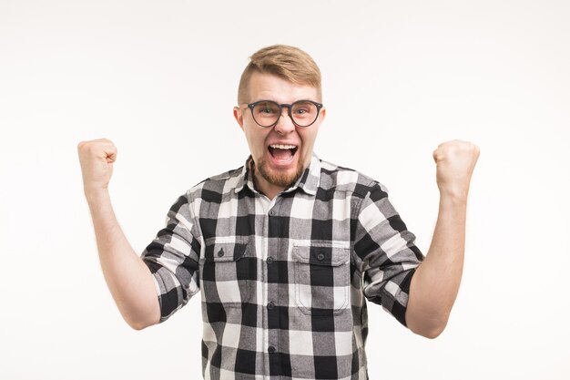 Foto concetto di persone, emozioni e trionfo - giovane eccitato e felice vestito in camicia che mostra i pugni sulla superficie bianca.