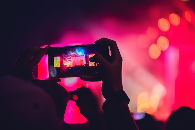 People enjoying rock concert and taking photos with cell phone at music festival.