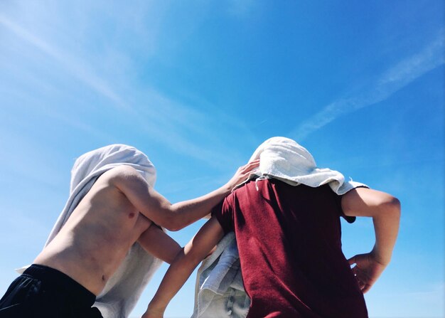 People face covered with t-shirts against blue sky