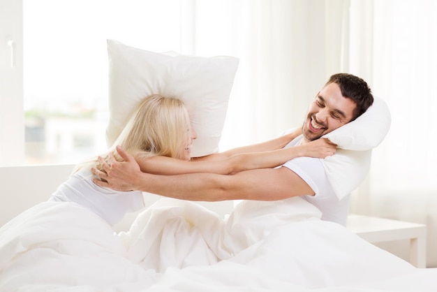 people, family, bedtime and fun concept - happy couple having pillow fight in bed at home