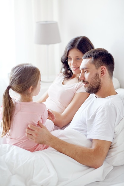 people, family and morning concept - happy child with parents in bed at home