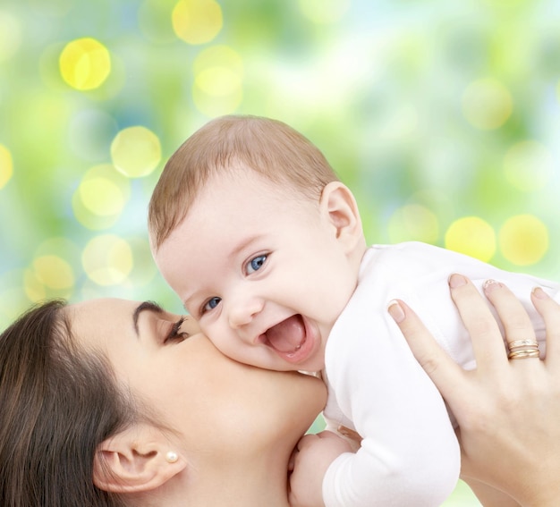 人々、家族、母性と子供の概念-緑のライトの背景に愛らしい赤ちゃんを抱き締める幸せな母