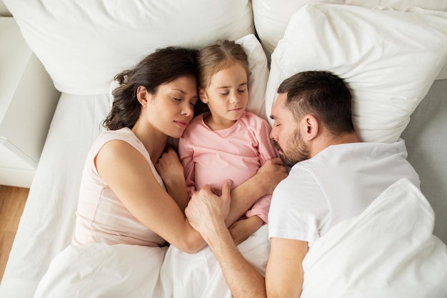 人、家族、休息のコンセプト – 自宅のベッドで両親が寝ている幸せな子供