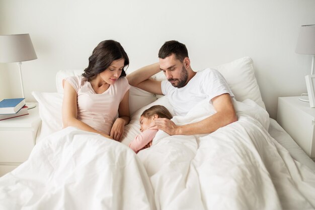 people, family and rest concept - happy child with parents sleeping in bed at home