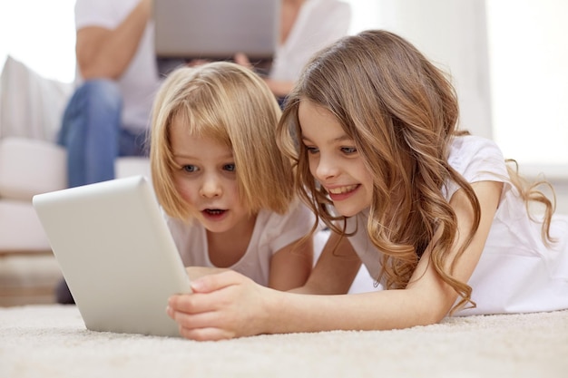 people, family, technology and children concept - happy little girls playing with tablet pc computer at home