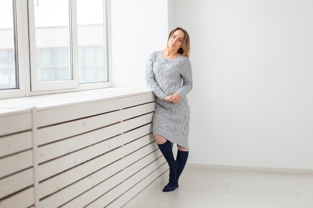 People and fashion concept - Beautiful dreaming woman in knitted dress near a sill.