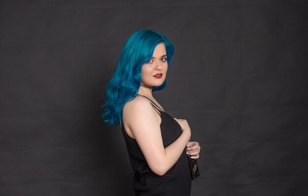 People and fashion concept - Woman dressed in black dress and blue hair posing over black background with copy space