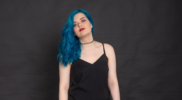 People and fashion concept - Woman dressed in black dress and blue hair posing over black background with copy space