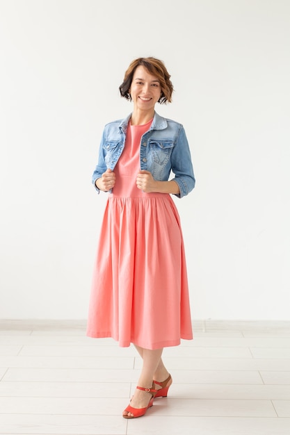 people, fashion and style concept - young woman posing in clothes in studio on white wall