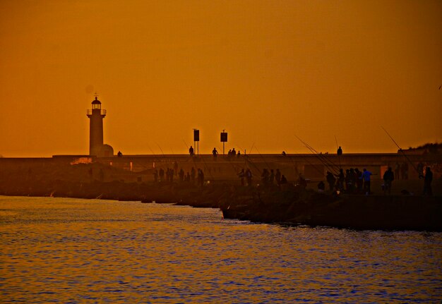 People fishing by sea against clear sky