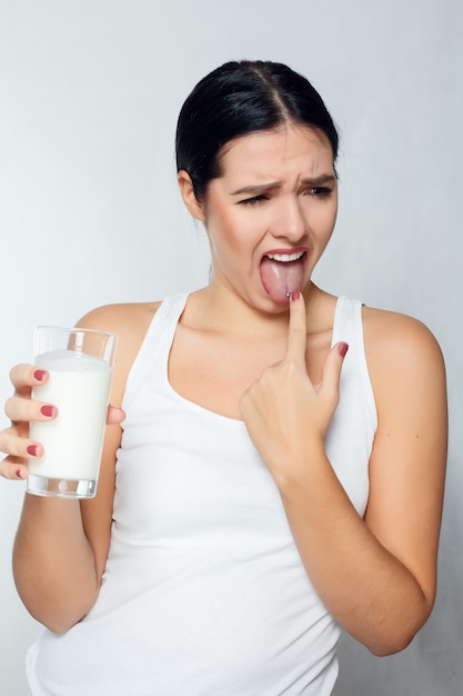 People, food, beauty, lifestyle, fashion and sensitive concept - Expression of a brunette girl holding a glass of milk, dairy product and do not like to drink it