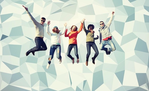 people, freedom, happiness and teenage concept - group of happy friends in sunglasses jumping high over gray low poly background