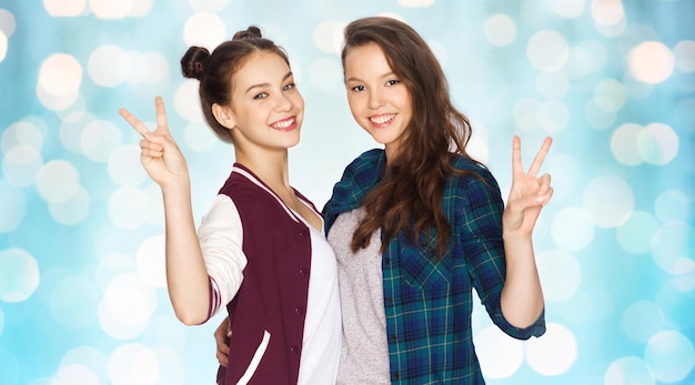 Photo people, friends, teens and friendship concept - happy smiling pretty teenage girls hugging and showing peace hand sign over blue holidays lights background