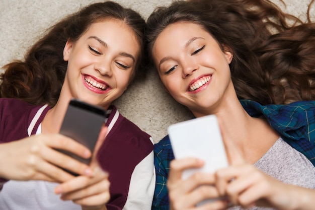 people, friends, teens and friendship concept - happy smiling pretty teenage girls lying on floor with smartphones