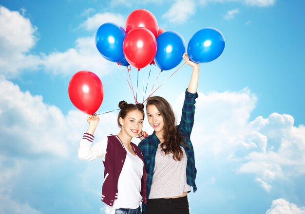 people, friends, teens, holidays and party concept - happy smiling pretty teenage girls with helium balloons over blue sky and clouds background