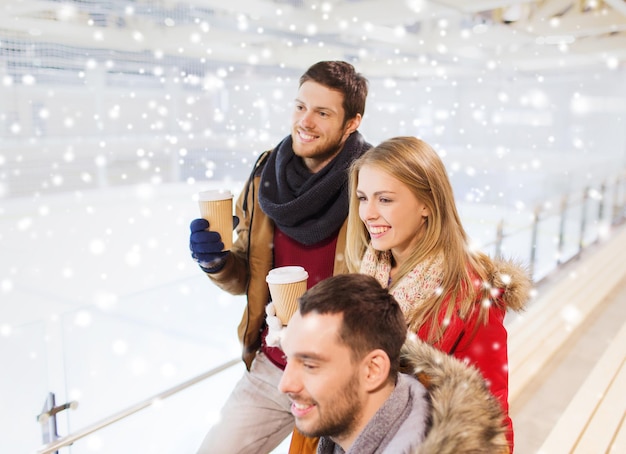 people, friendship, hot drinks and leisure concept - happy friends drinking from paper coffee cups on skating rink