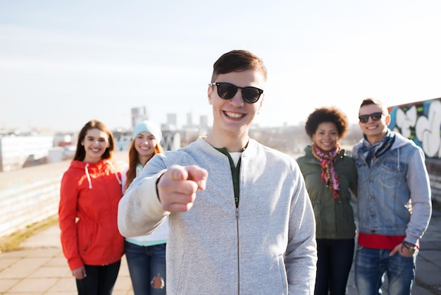 people, friendship and international concept - happy young man or teenage boy pointing finger to you in front of his friends on city street