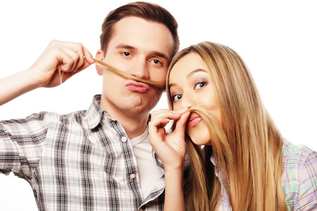 People, friendship, love and leisure concept. beautiful young loving couple making fake moustache from hair while standing isolated on white.