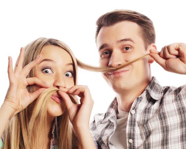 People, friendship, love and leisure concept - beautiful young loving couple making fake moustache from hair while standing isolated on white.