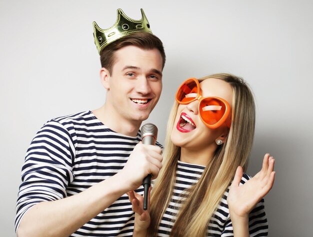 People friendship love and leisure concept beautiful young loving couple with microphone Big orange glasses and crown Ready for party