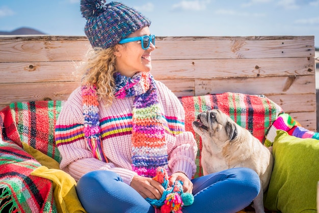 People in friendship and love with dog animals happy and\
cheerful pretty young lady enjoy time and have fun with her best\
friend dog pug in outdoor winter leisure activity concept of life\
together