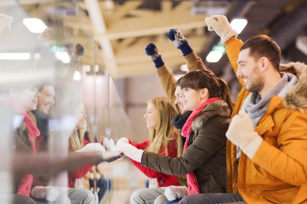 people, friendship, sport and leisure concept - happy friends watching hockey game or figure skating performance on skating rink