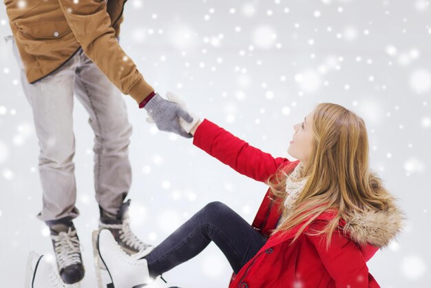 people, friendship, sport and leisure concept - smiling man helping women to rise up on skating rink