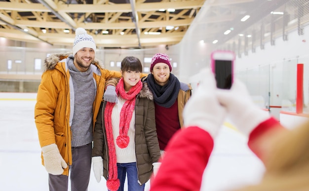 people, friendship, technology and leisure concept - happy friends taking photo with smartphone on skating rink