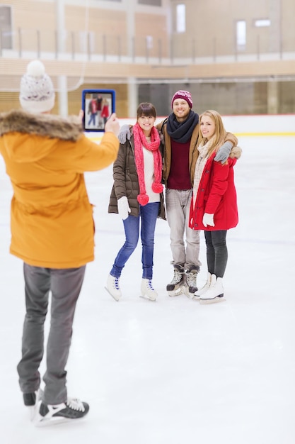 people, friendship, technology and leisure concept - happy friends taking photo with tablet pc on skating rink