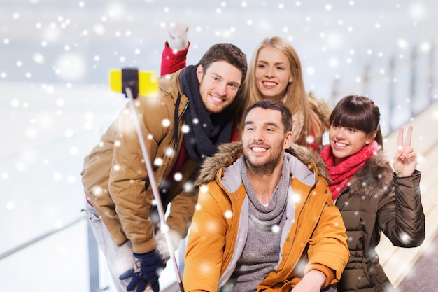 people, friendship, technology and leisure concept - happy friends taking picture with smartphone selfie stick on skating rink