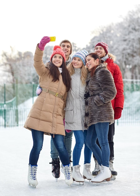 people, friendship, technology and leisure concept - happy friends taking selfie with smartphone on ice skating rink outdoors