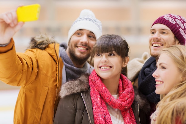 people, friendship, technology and leisure concept - happy friends taking selfie with smartphone on skating rink