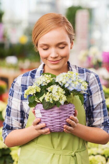 人、ガーデニング、職業のコンセプト – 幸せな女性や庭師が温室で花の匂いを嗅ぐ