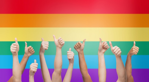 사람들, 게이 프라이드, 제스처 및 동성애 개념 - 무지개 깃발 줄무늬 배경 위에 엄지손가락을 보여주는 인간의 손