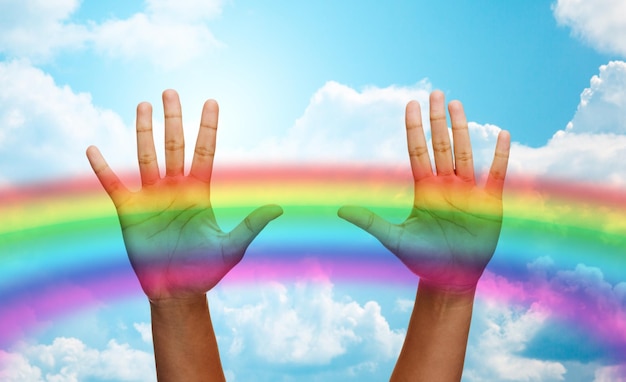 people, gay pride and homosexual concept - palms of african american human hands over rainbow in blue sky background