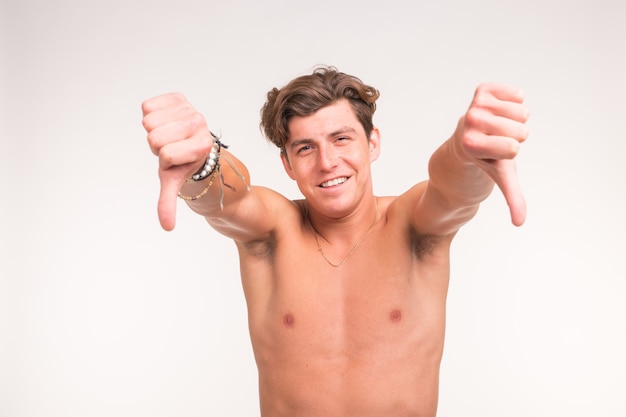 Концепция людей, жестов, фитнеса и спорта - атлетичный мужчина без рубашки показывает большие пальцы руки вниз над белой поверхностью.