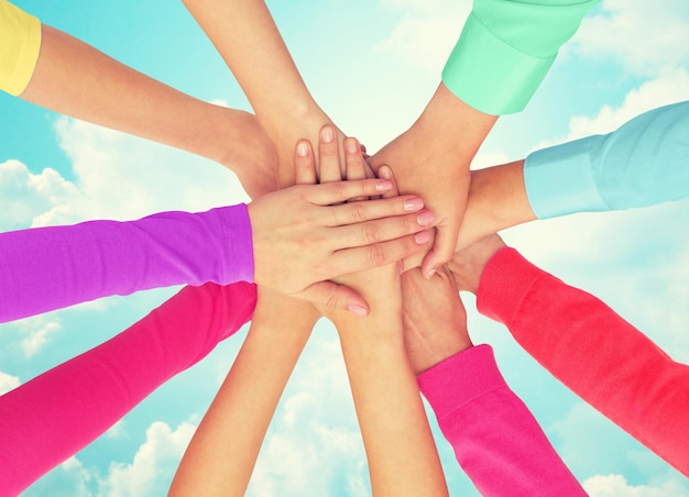 people, gesture, gay pride and homosexual concept - close up of women hands in rainbow clothes on top of each other over blue sky background