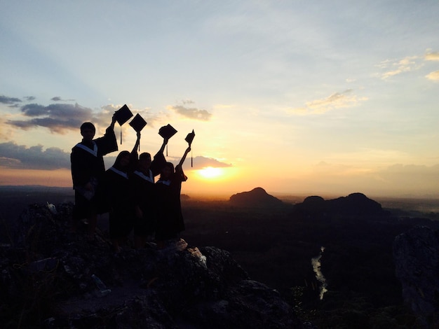 Foto persone in abito da laurea in montagna contro il cielo durante il tramonto